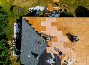 A worker applies a white protective coating to a low-slope roof beside roofing tools and drainage equipment.