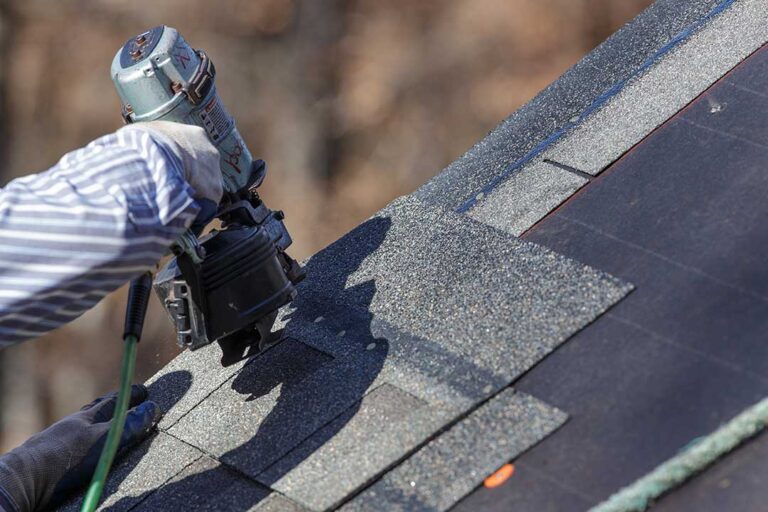 Uneven shingles and loose flashing are visible on a residential roof beside a damp attic ceiling.